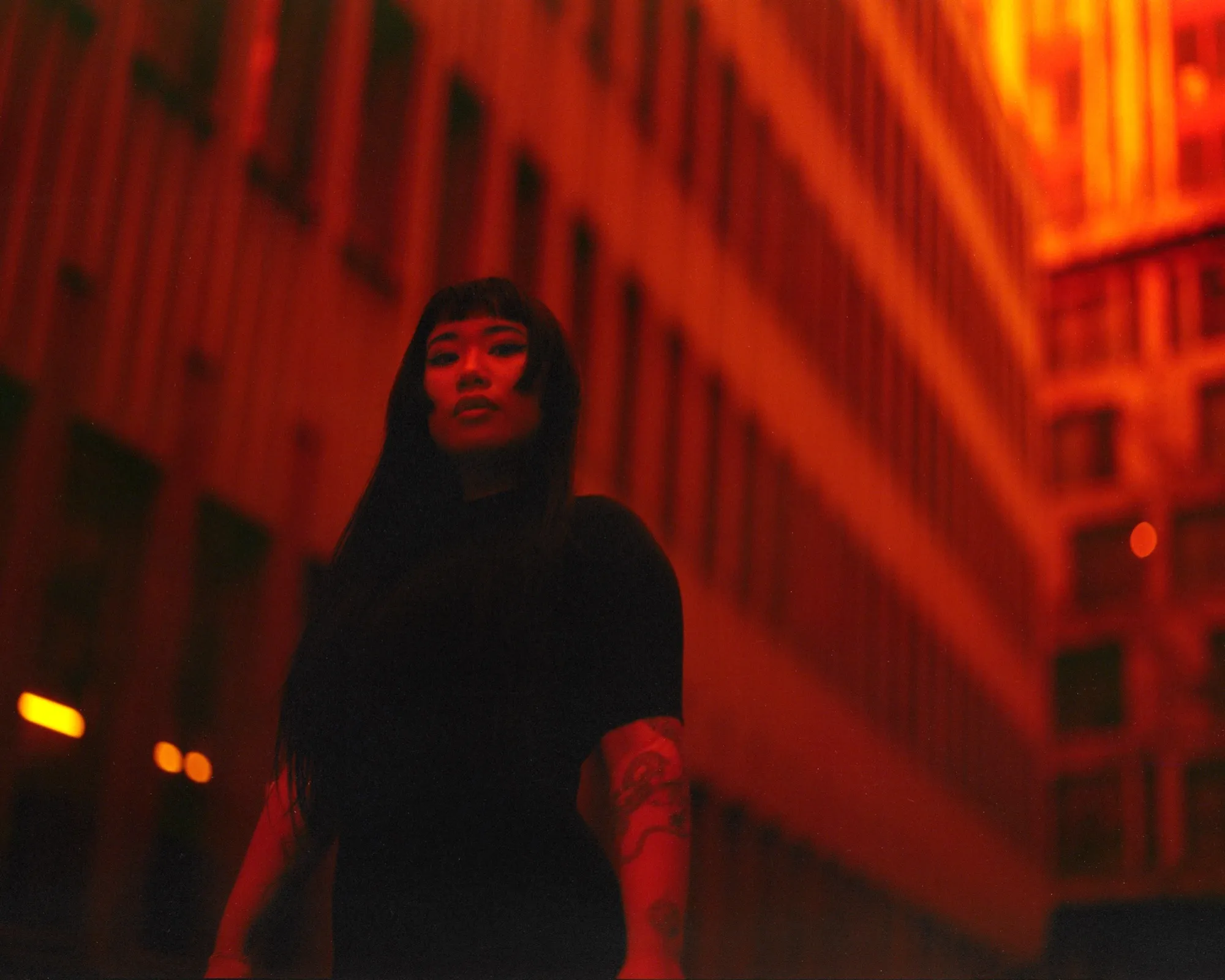 A woman between office towers bathed in deep red light