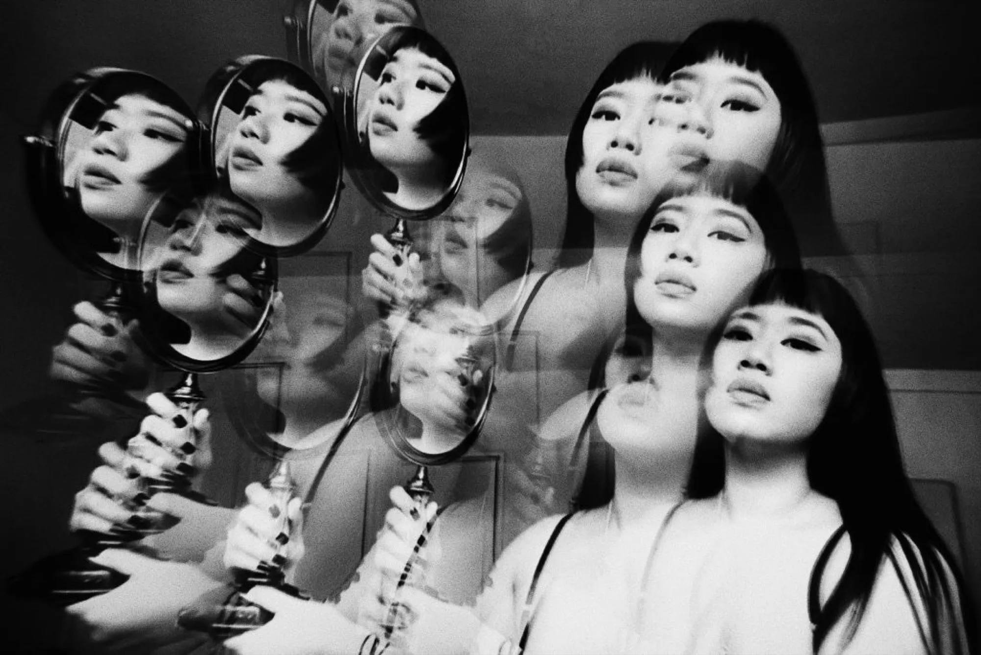 Black-and-white multiple exposure with a hand mirror, faces repeating across the frame