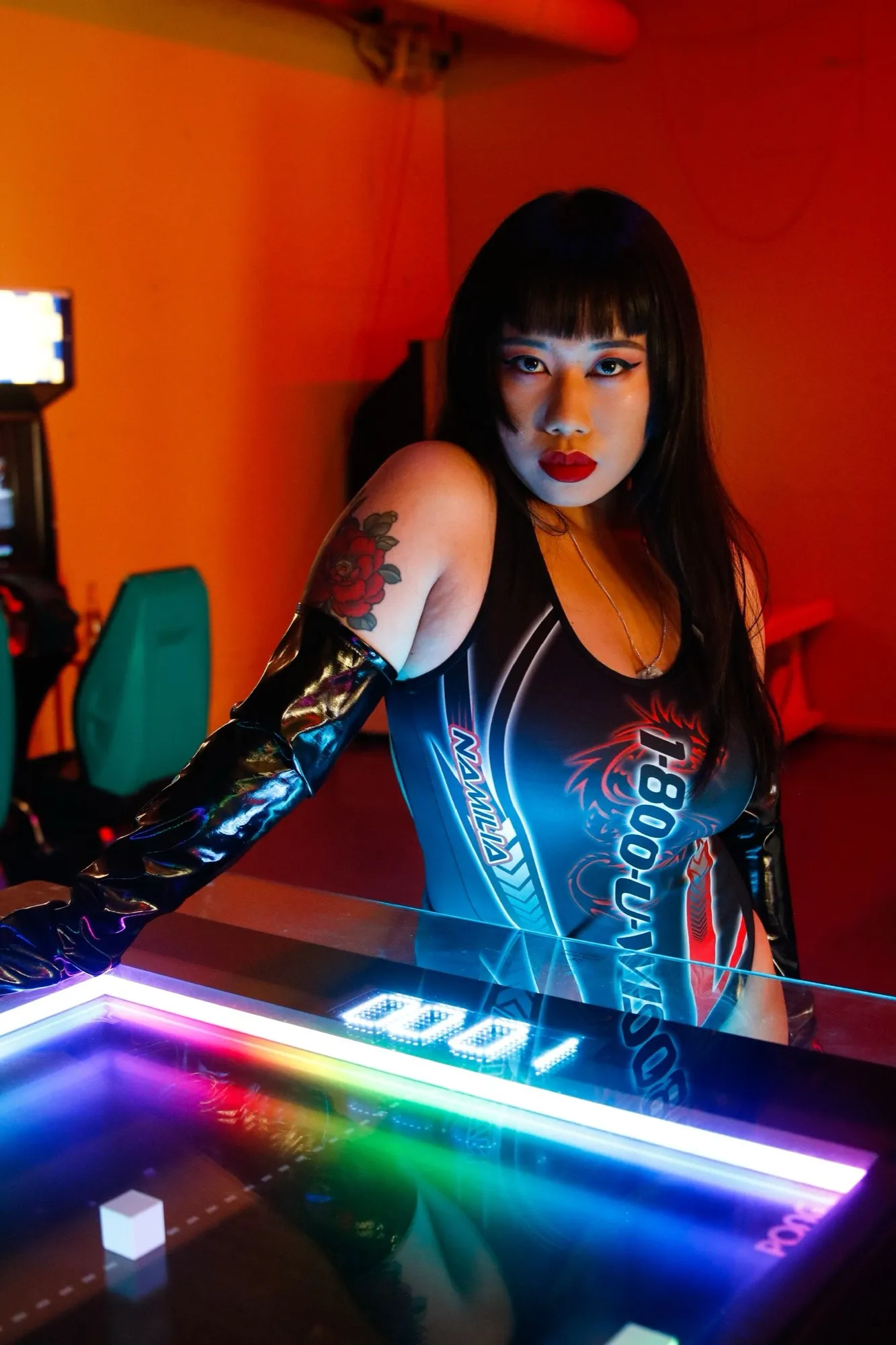 Self-portrait at an arcade air-hockey table in neon light, racer suit and long black hair