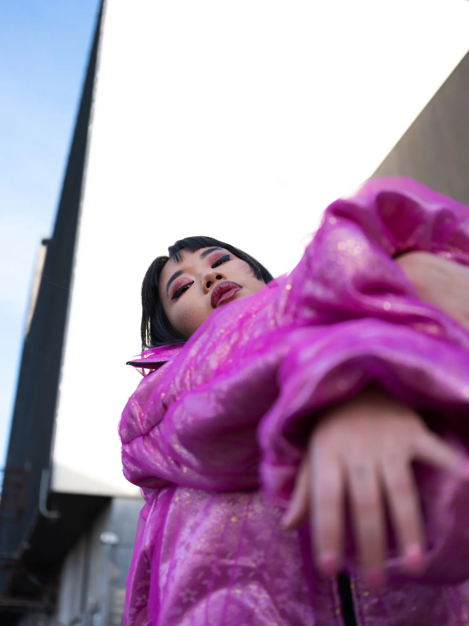 Low-angle portrait in a shining magenta jacket against the sky, for Concrete Store