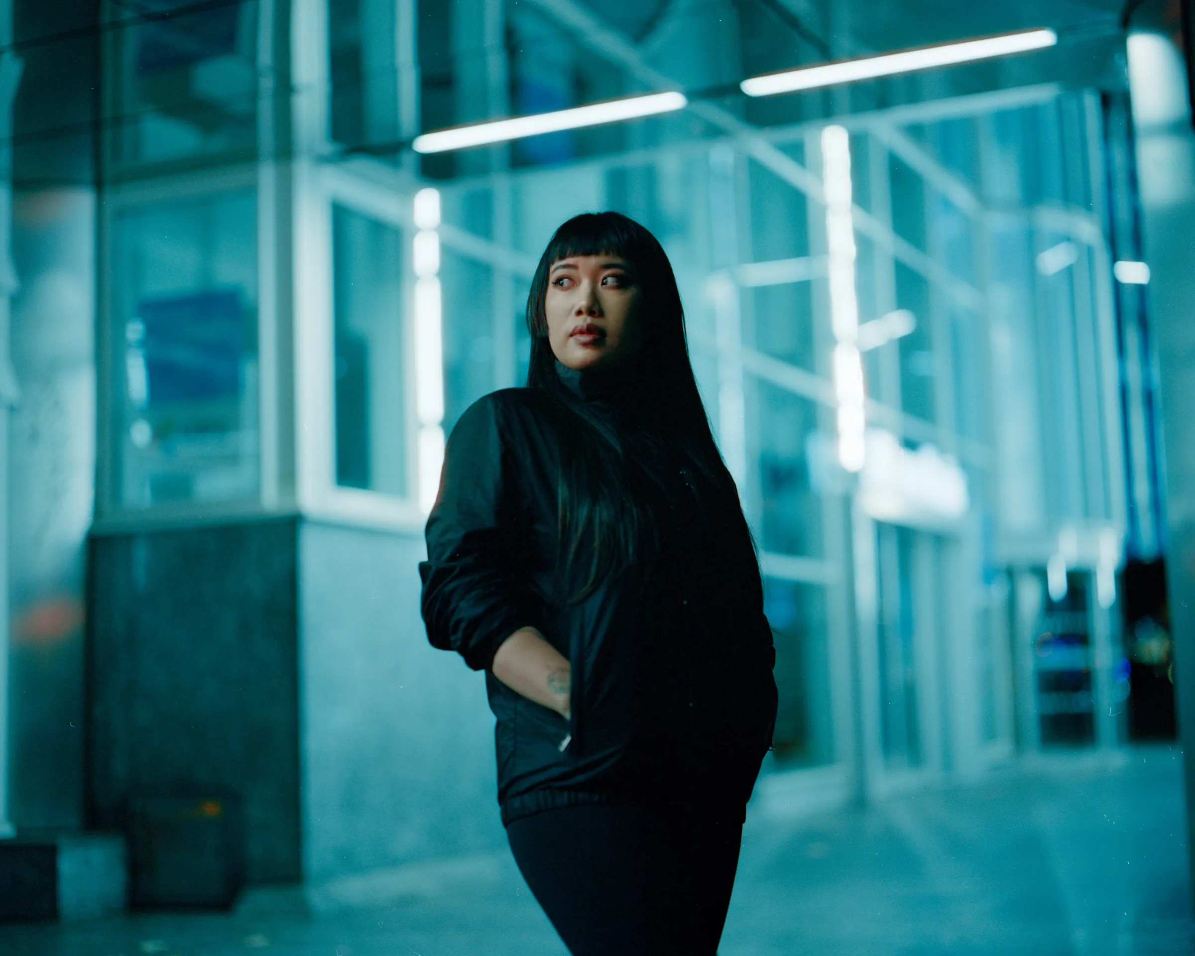 Xiang Yu Yeung at night, lit in teal by a storefront window