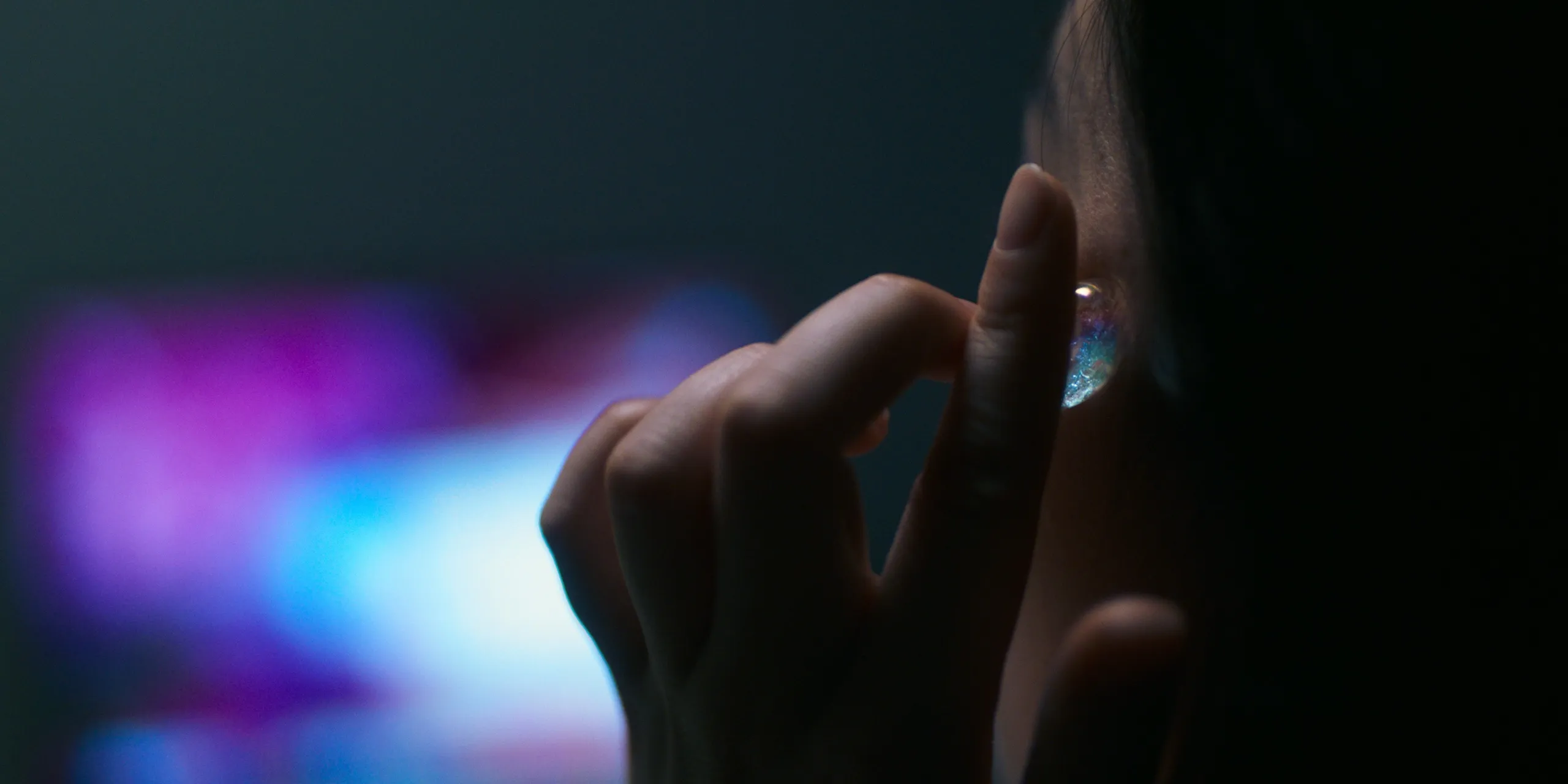 Ami puts in an earbud, the virtual world glowing on a screen behind her