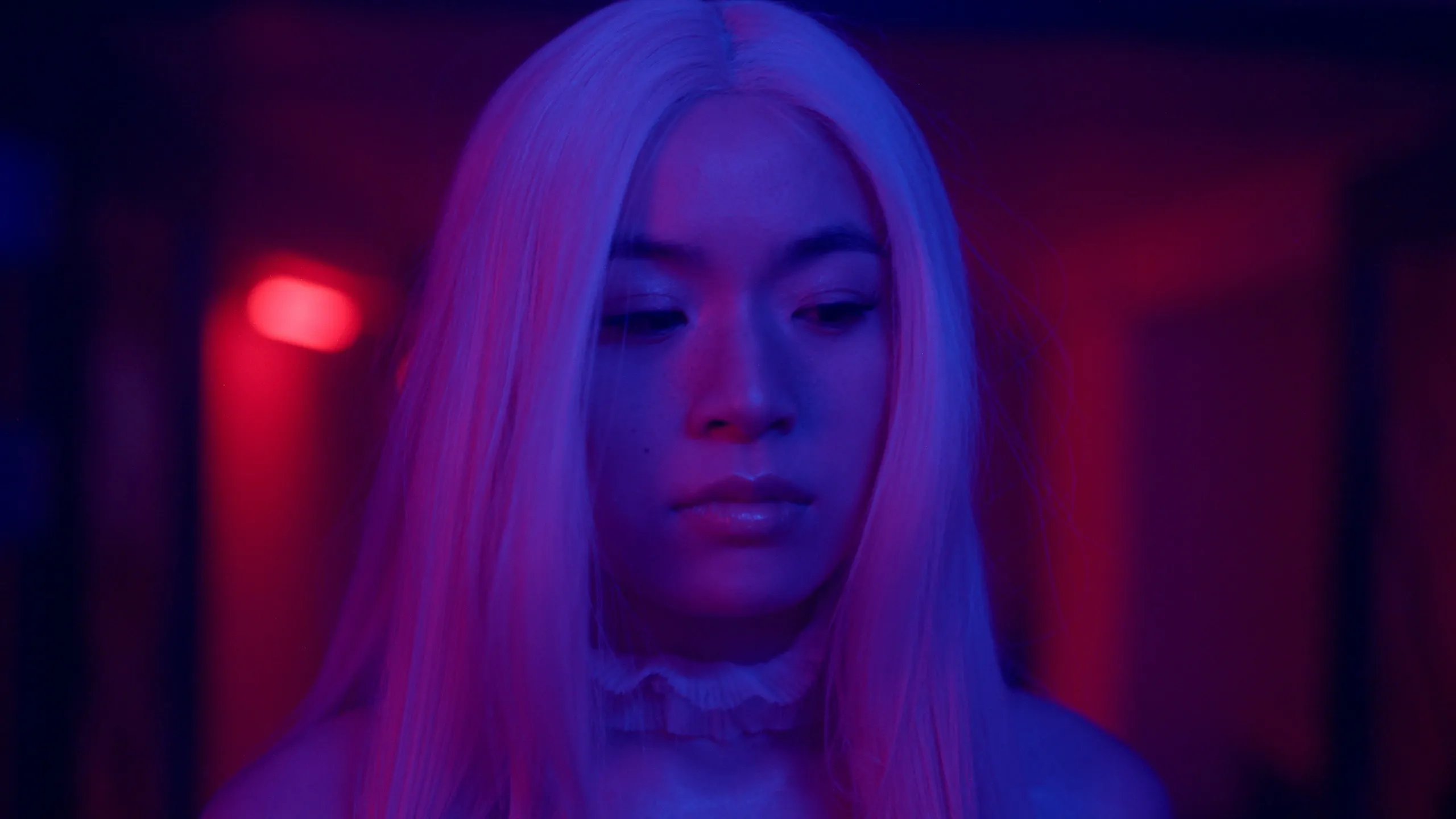 The alter ego, pink-haired, lit in red and blue neon